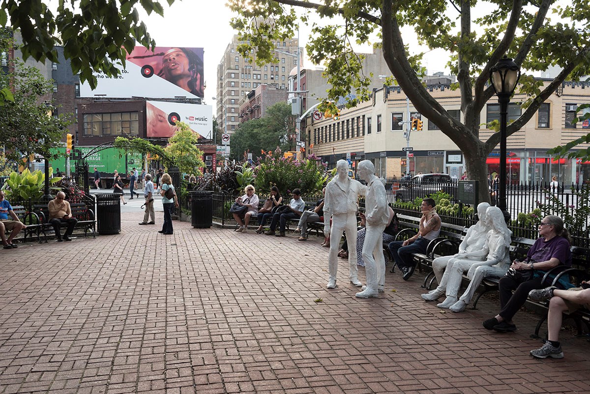 People sit on benches around the perimeter of a brick plaza at Christopher Park