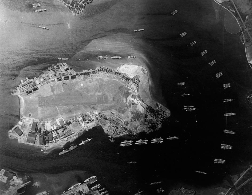 Aerial photograph of Ford Island, 1940. Structures line the edge of the island, and a formation of ships partially surrounds the island