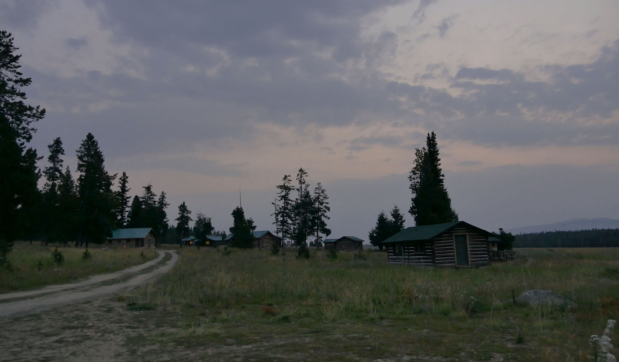 Dim sky over a landscape with small cabins, scattered trees, and a curving gravel road