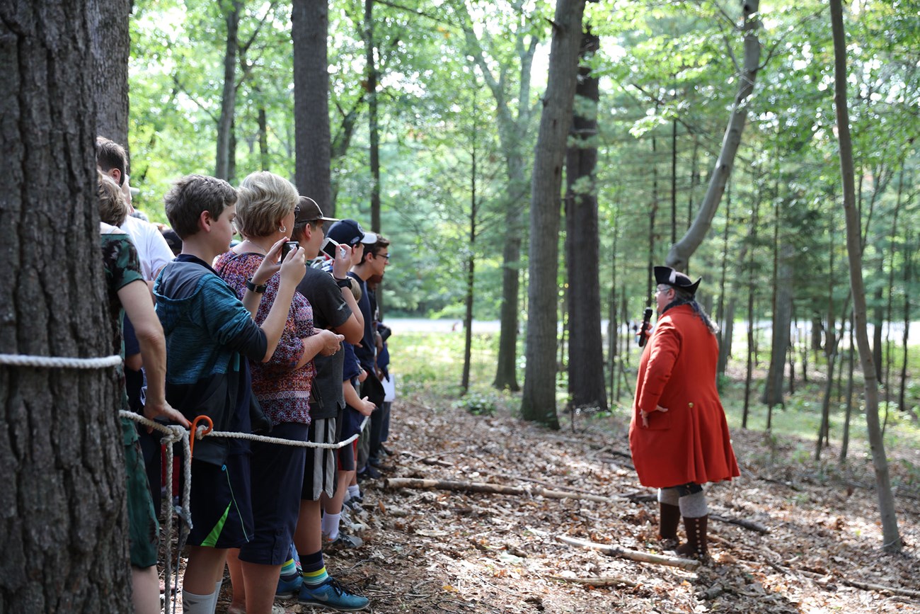 A British Regular soldier reenactor holds a microphone to address a crowd of visitors