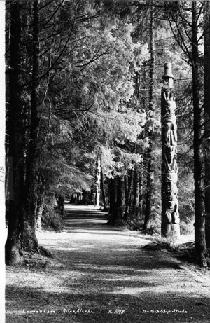 A black and white photo of "Lover's Lane," where totem poles line a forest walk.