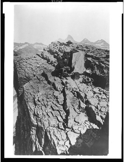 Two men stand with camera equipment on a rocky mountaintop.