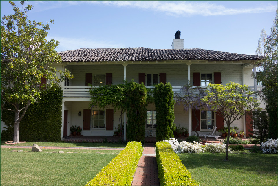 A hedge-lined walk leads to a two-story house, with porches on both levels.
