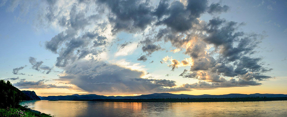 A sunset sky glows behind feathered gray clouds over a broad river