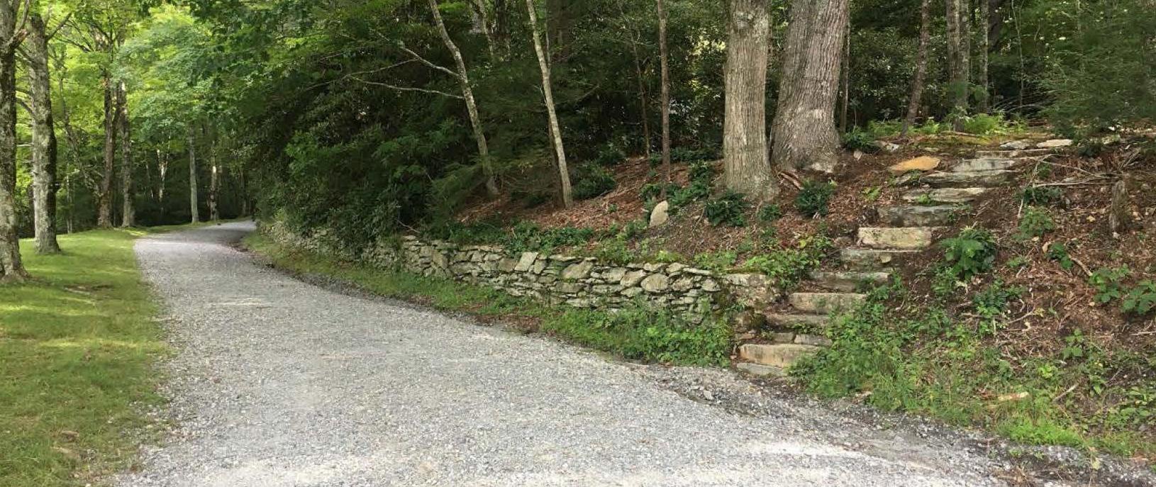 Stone stairs ascend a wooded hillside to the right of a gravel road