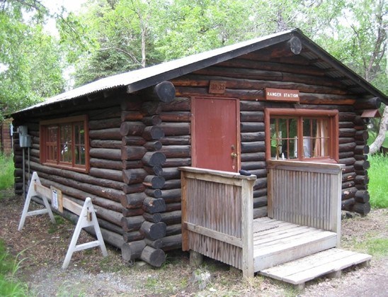 A one-story structure with saddle-notched logs, a small wooden porch, and a Ranger Station sign