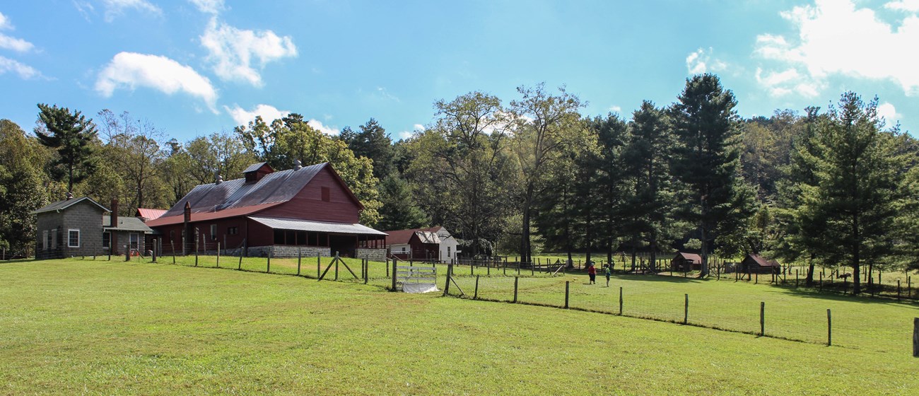 Wood and wire fencing creates pasture area in front of a barn and other farm buildings.