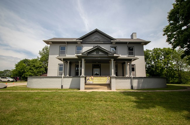 A two-story, rectangular house with a low wall wrapping around the front porch, surrounded by turf.