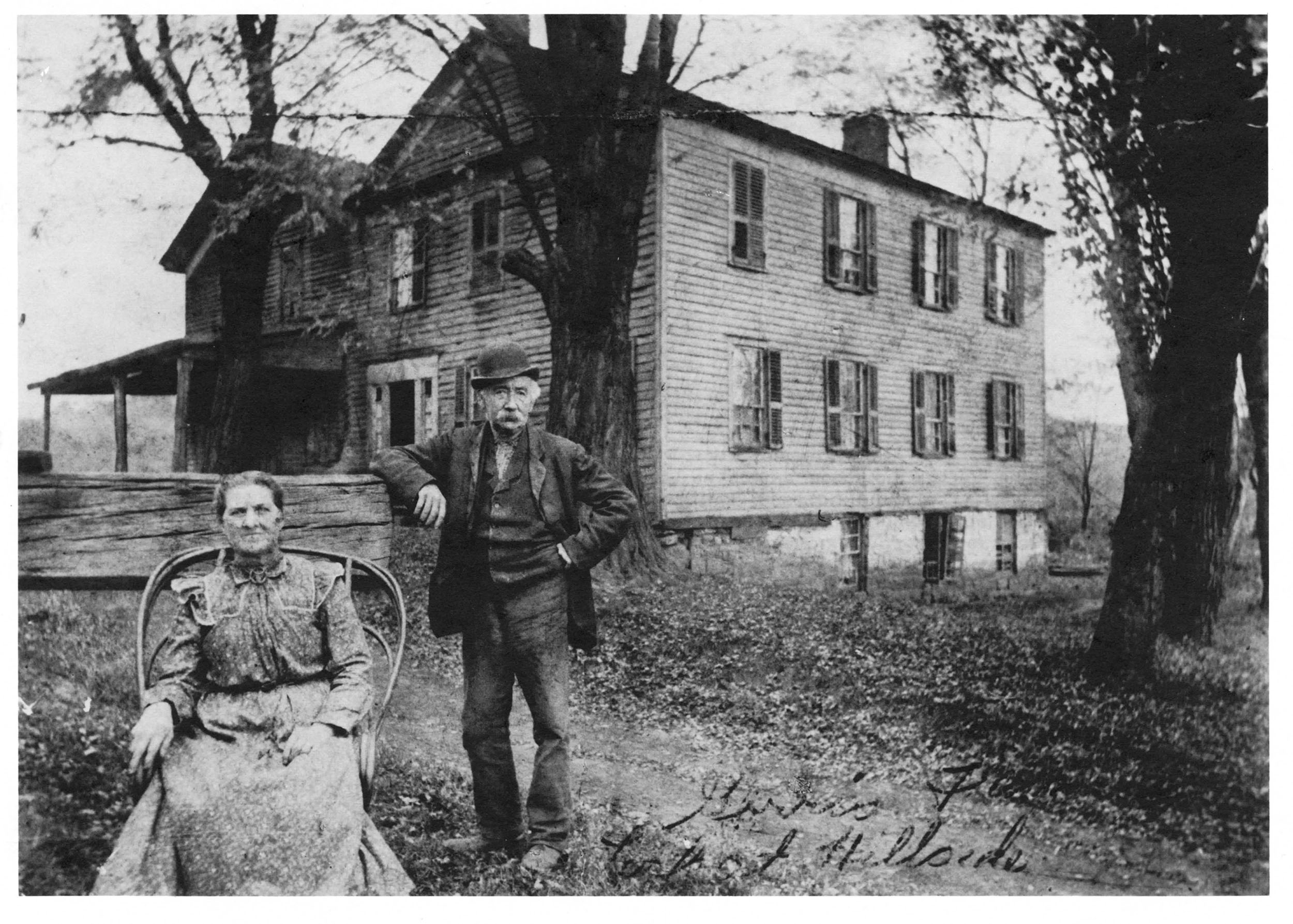 A man in a suit stands beside a seated woman outside of a two-story structure on the Ohio and Erie Canal, 1890
