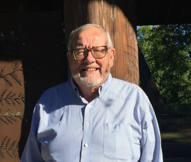 Dennis Lewarch stands in the sun beside a shaded pavilion at the Arboretum