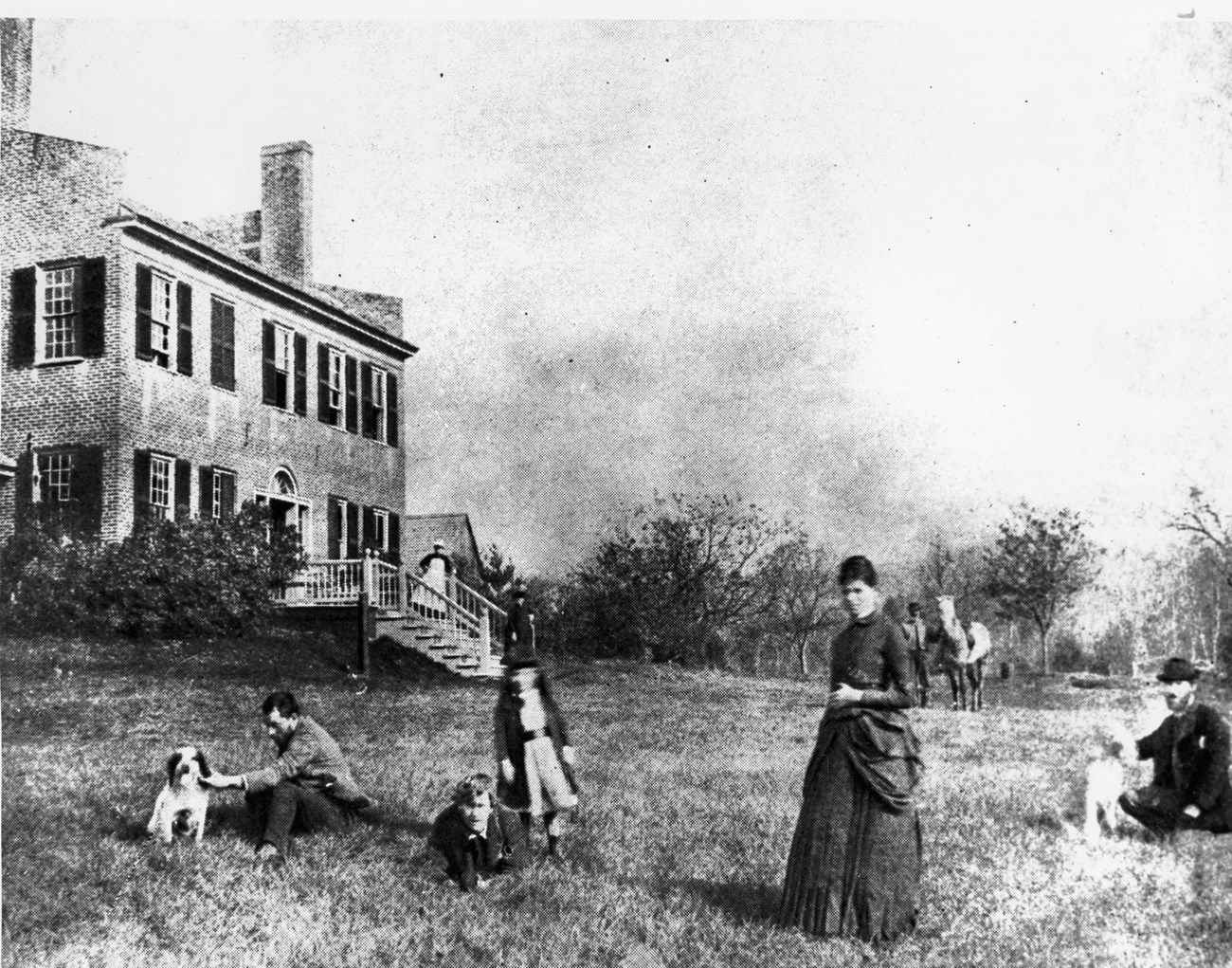 Saint-Gaudens (far right) during his first summer at Aspet with (from left to right) his brother Louis; Frederick, MacMonnies; his assisstant; his son, Homer; and his wife Augusta. The two-story house and fruit trees are in the background.