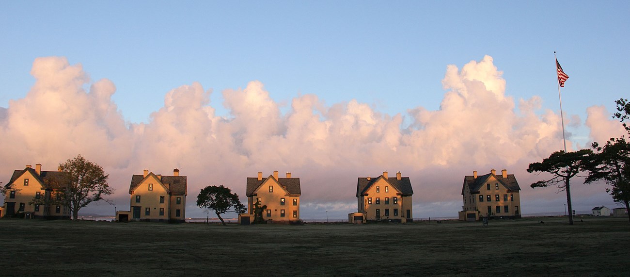 A row of five matching three-story buildings are evenly spaced along the edge of an open expanse of grass.