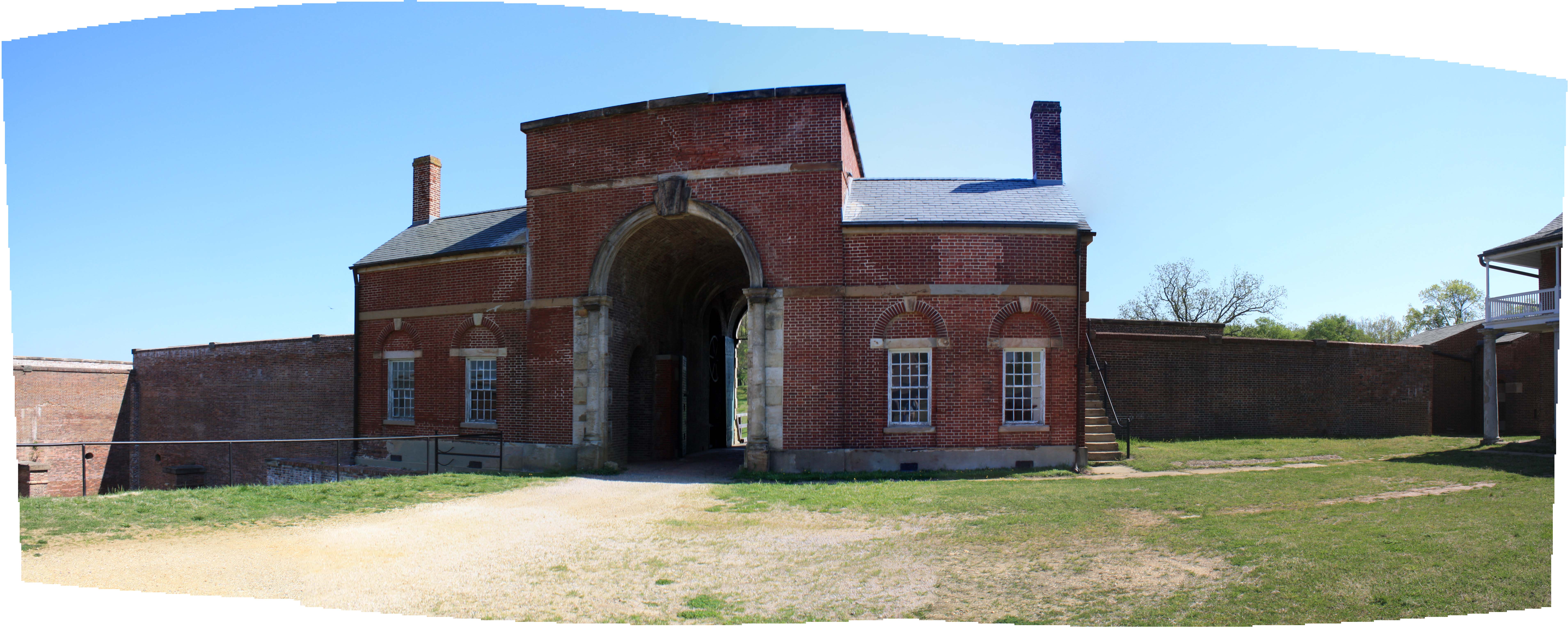 A tall archway opens through a red brick gatehouse in a brick wall