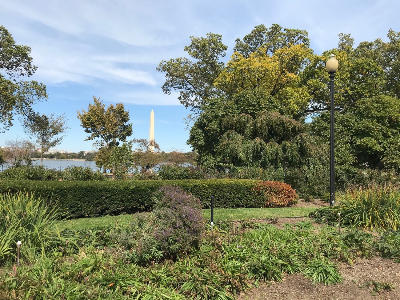 Flower beds, a low hedge, a trees of the George Mason Memorial with the Tidal Basin and Washington Monument in the background.