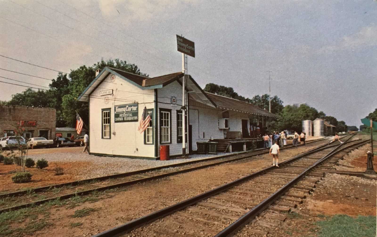 The side of the one-story train depot. a wooden structure with green trim, beside railroad tracks.