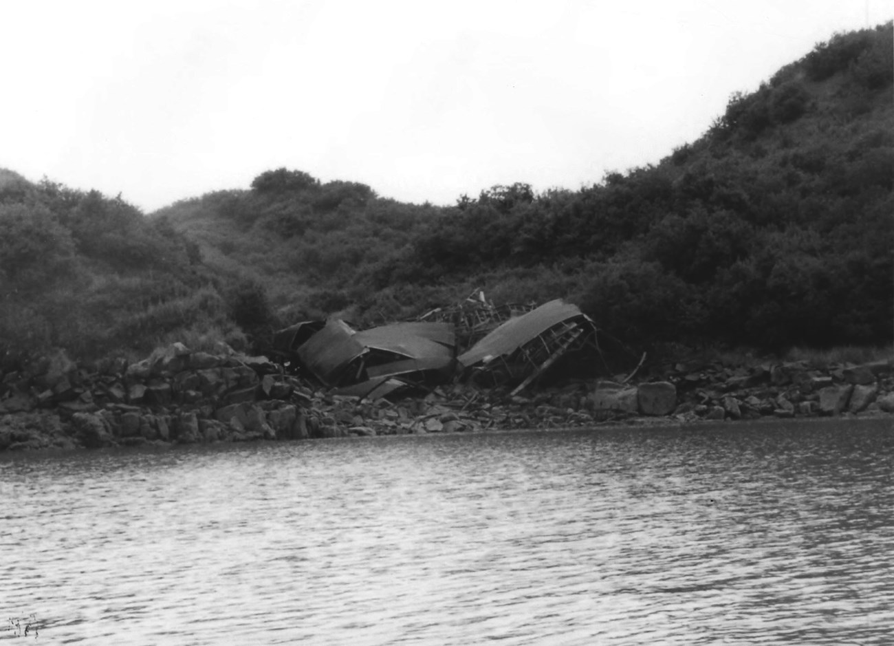 A collapsed structure on a rocky coastline, between water and rolling hills