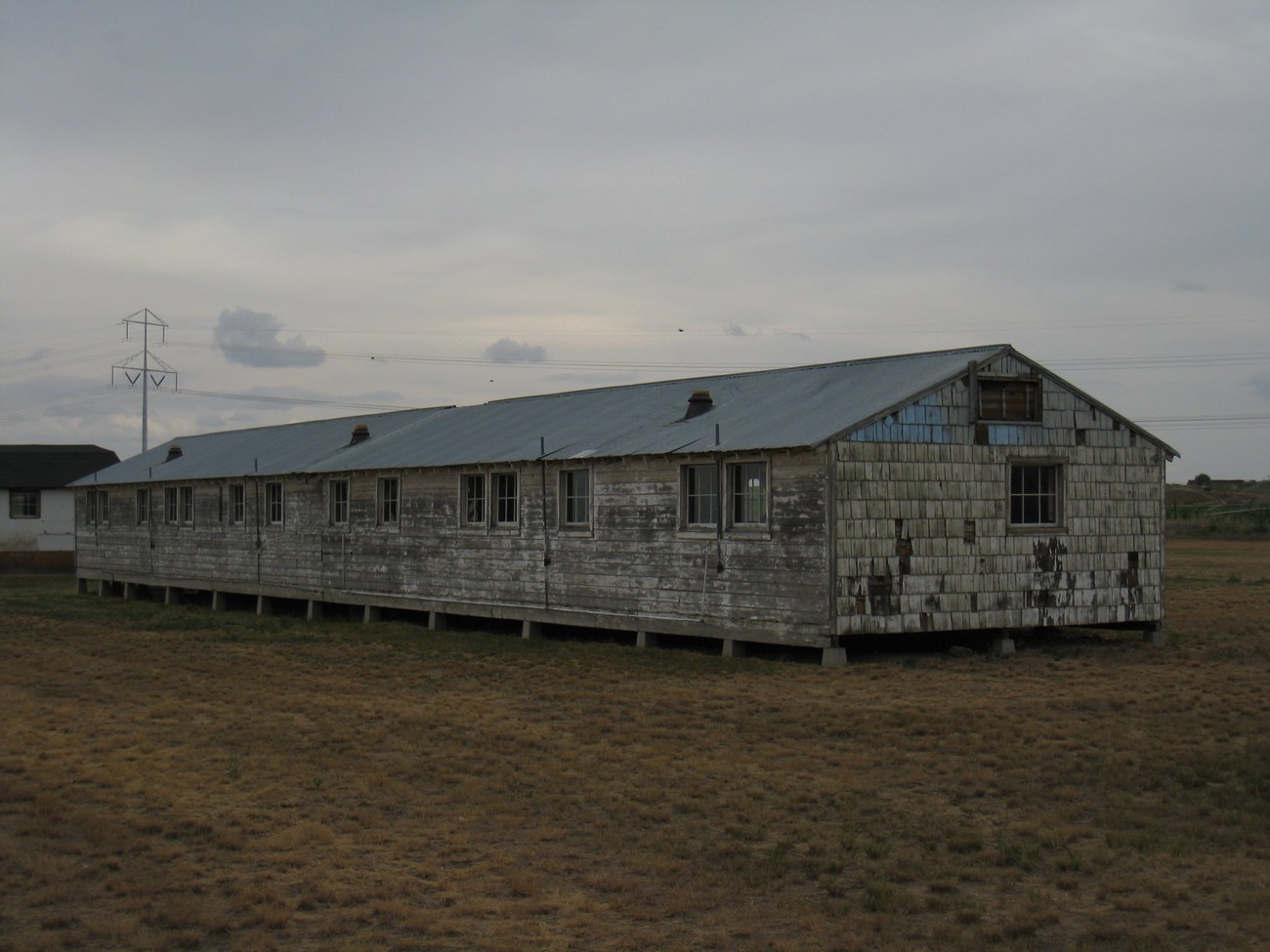 A long, one-story barrack building with worn timber siding, raised on concrete piers.