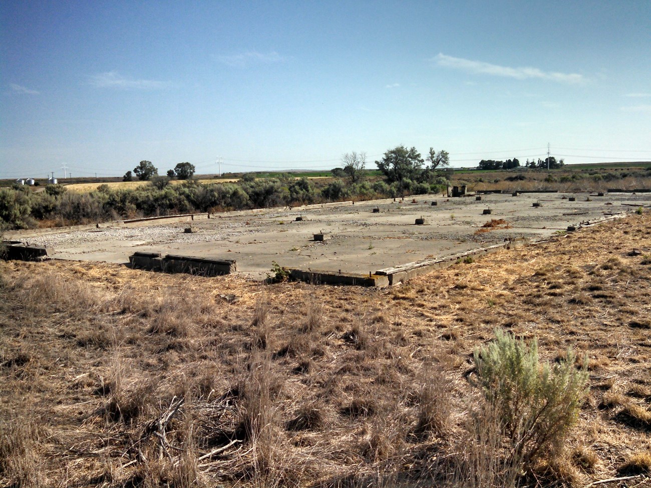 A large, rectangular building foundation is surrounded by dry grasses in an open landscape.