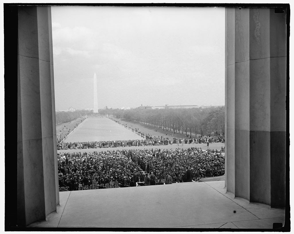 A view through columns from the Lincoln Memorial, showing a large crowd and the reflecting pool and Washington Monument in the background.