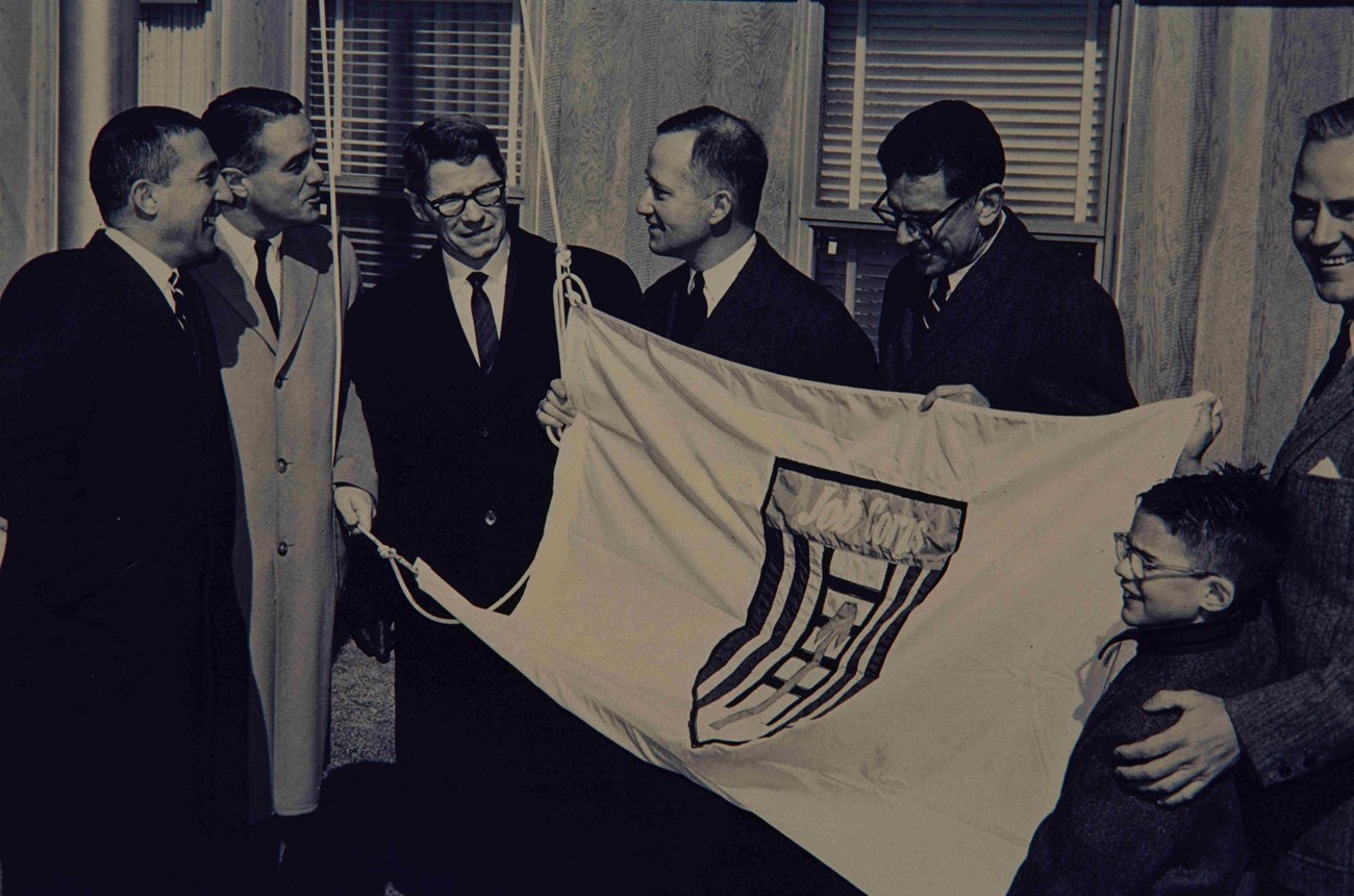 A group of men in overcoats and ties hold a white flag with the Job Corps logo