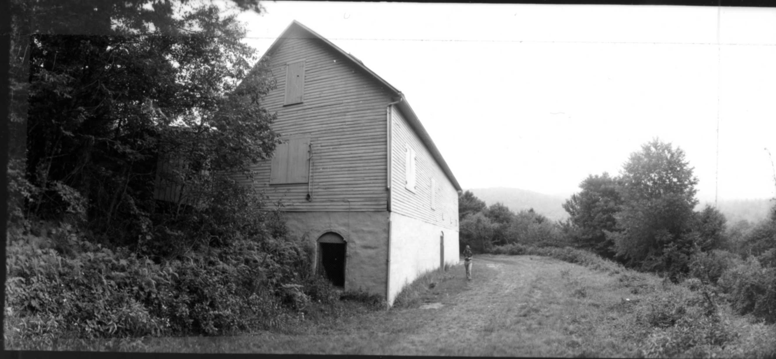 Trees and grasses grow beside a long two-story barn with several windows and an awning.