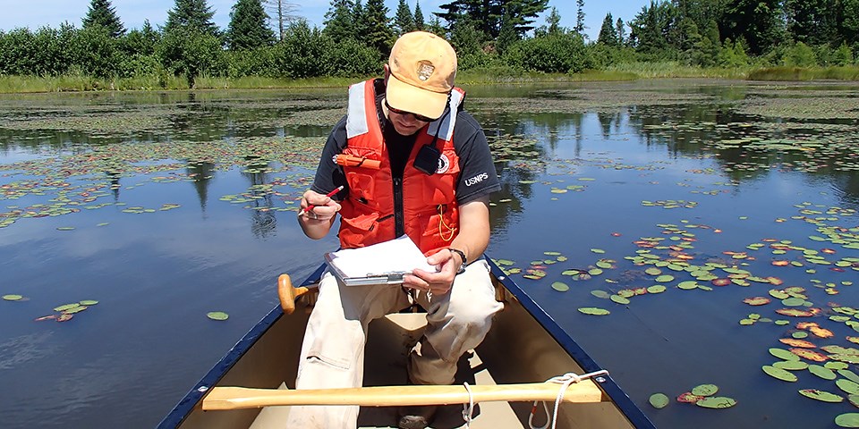An NPS employee sits in a boat, he is writing on paper