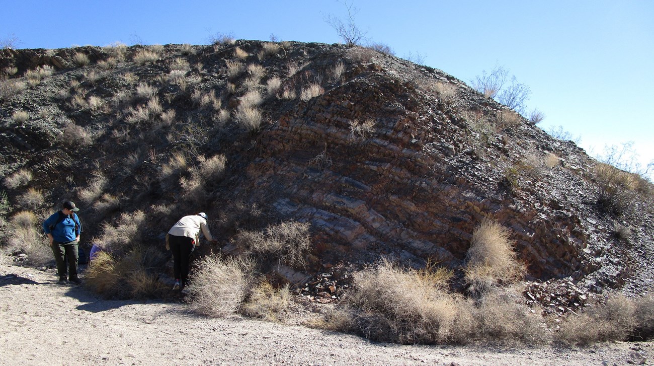 Photo of two people exploring a rock outcrop with banded layers