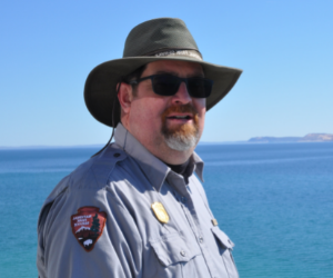 park ranger poses for picture with water in background
