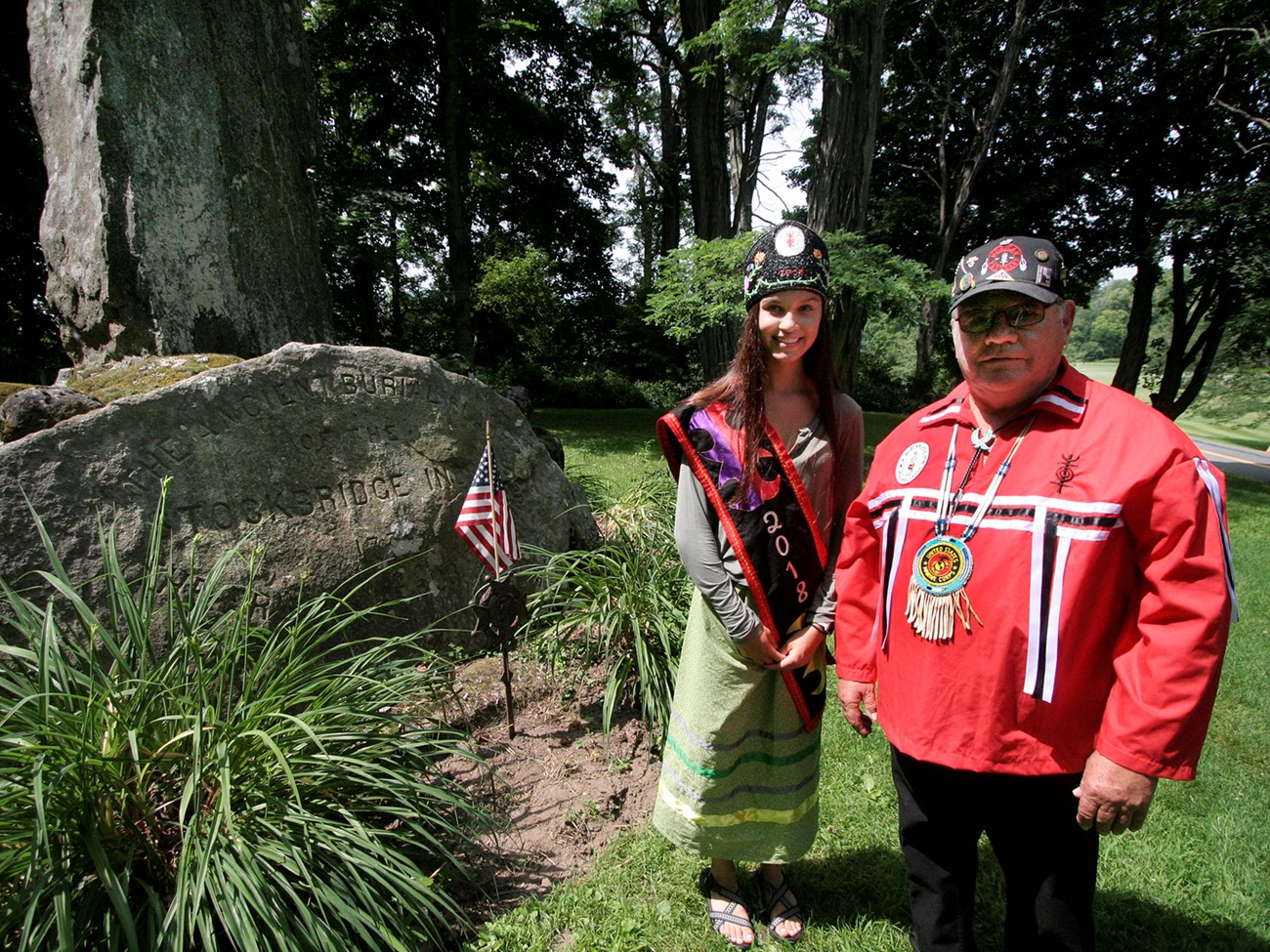 Odessa Arce and Robert Little stand next to the stone pillar monument at the Stockbridge Indian Burial Ground