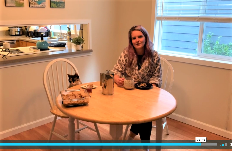 A woman and a cat sit at a breakfast table with a pan of breakfast bars cooling on the table.