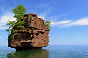 A large rock stands in the water with trees growing on it