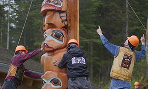 Three men work to place a totem pole upright