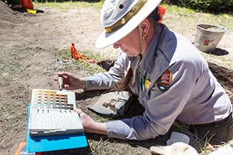 Beth Horton in her NPS uniform and soft field hat uses a color chart to classify soils.