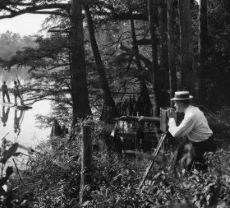 Man in the Everglades with an old movie camera films two men in a canoe