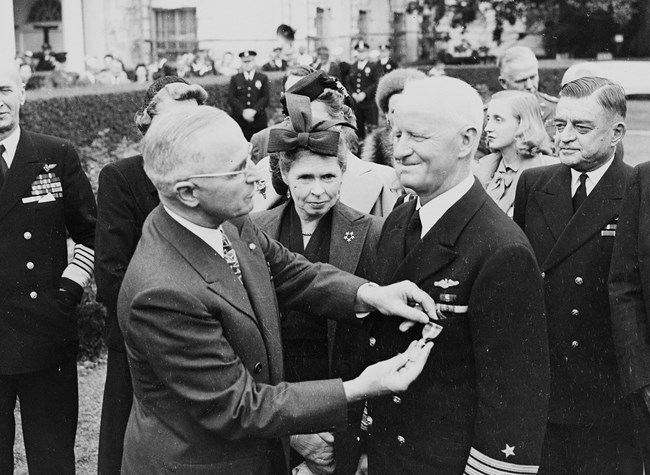 President Truman pins a gold star on Admiral Nimitz amidst a crowd standing outside the White House