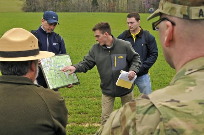Man points out places on a park map to military staff on a tour.