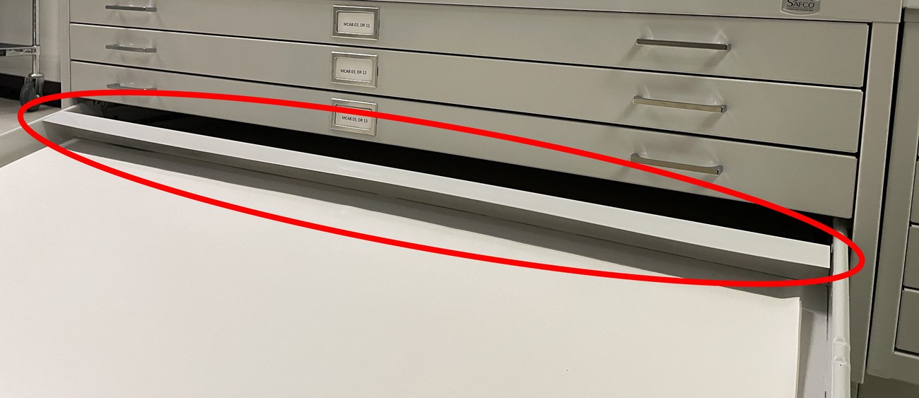 An open flat file drawer with a red circle pointing out the rear drawer hood.