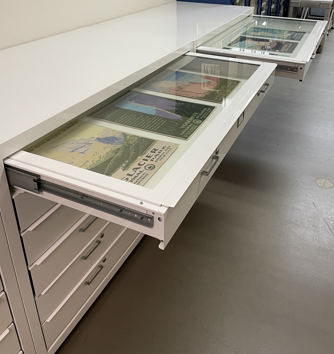 White flat file units with the top drawers pulled out to show the WPA posters inside.