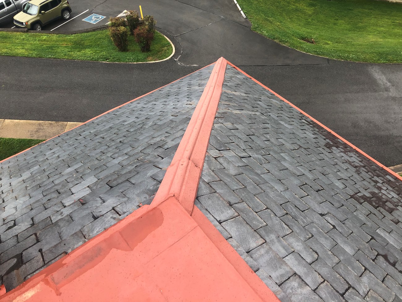 Slate shingles on two sides of a roof come together at a ridge, seen from overhead looking down to the driveway