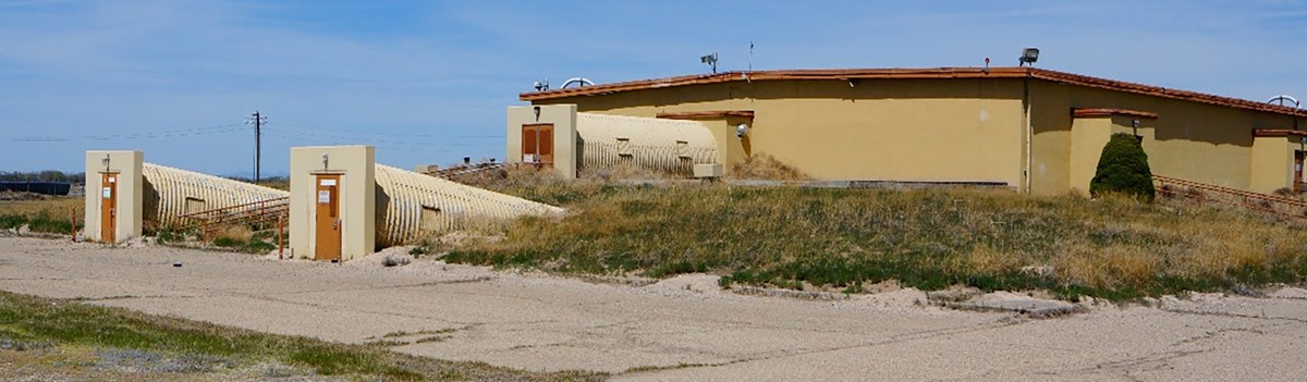 A yellow concrete building is low on the ground with doors coming from three tubes connected to one side.