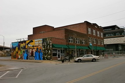 A row of brick buildings along a street. The side of the one facing the camera is covered in a mural depicting historical figures.