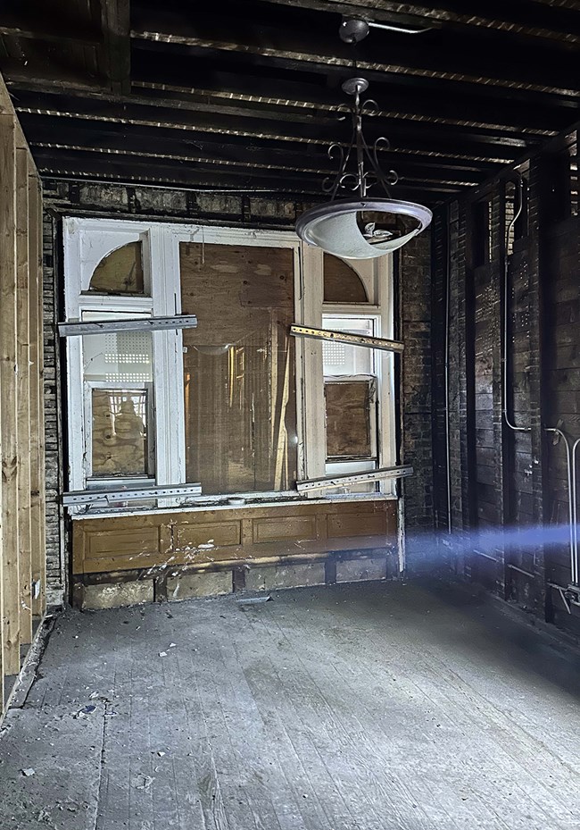 Image of the interior of a house, with exposed beams and studs, and a boarded-up window.