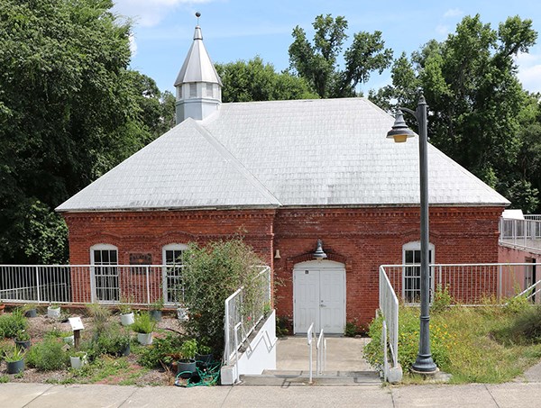 Image of brick building, concrete sidewalk and steps, railings, and plants.