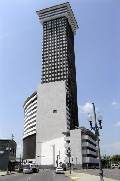 Image of tall white and brown building, streets, sidewalks, and cars.