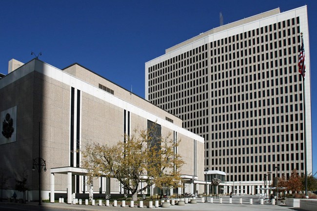 A broad, five-story courthouse set perpendicular to an 18-story office tower, both of which frame an open plaza at the southeastern corner of the property