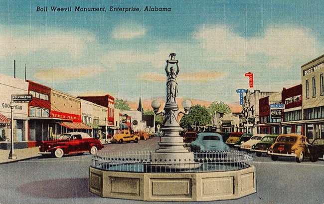 Color postcard showing image of statue in pool, buildings, road, and cars.