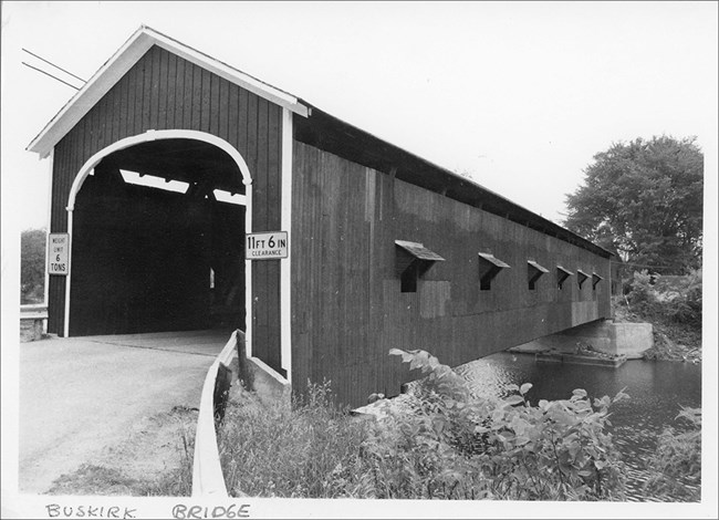 Image of wooden covered bridge, road, and water.