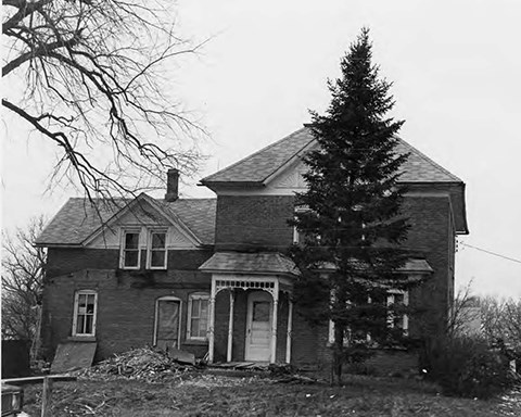 Image of brick house, lawn, trees, and sky.