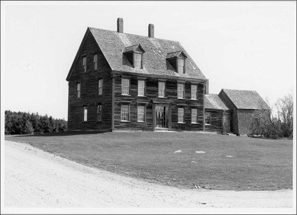 Image of a house with outbuildings, lawn, and unpaved road.