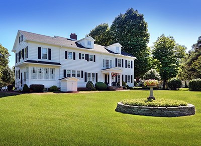 A large white two story historic house with a lawn in front.